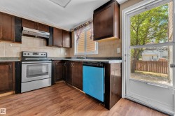 Kitchen featuring wood-finish flooring, dark wood cabinetry, stainless steel range and range hood, a tiled backsplash, and stone-look countertops - 