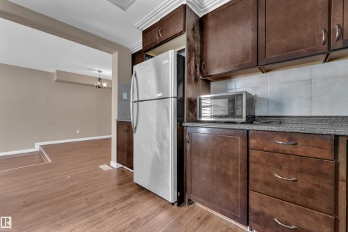 Kitchen featuring wood-finish flooring, dark wood cabinetry, and a light-colored tile backsplash - 6632 36A Avenue, Edmonton, AB 