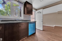 Kitchen area featuring wood-finish flooring, dark wood cabinetry, a double basin sink, and a window with natural light - 