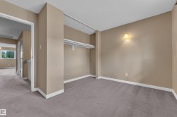 Spacious interior room featuring neutral-toned walls, gray carpeting, white baseboards, and a built-in closet shelving unit - 