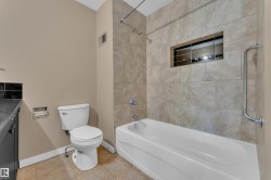 White soaking tub with subway tile surround featuring an integrated niche, chrome grab bar, and wall-mounted shower head - 