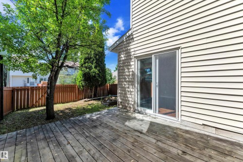 Expansive wood deck with direct access through a sliding glass door, complemented by light-colored horizontal siding, a private wood fence, and mature trees - 6632 36A Avenue, Edmonton, AB 