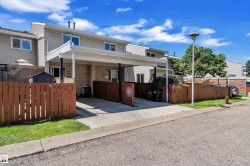 Vinyl-sided townhome featuring a covered carport, concrete driveway, and fenced front yard - 