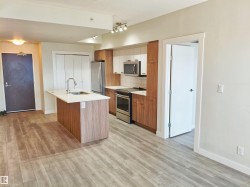 Open-concept kitchen and living area featuring wood-finish flooring, a kitchen island with sink, stainless steel appliances, and two-tone cabinetry - 