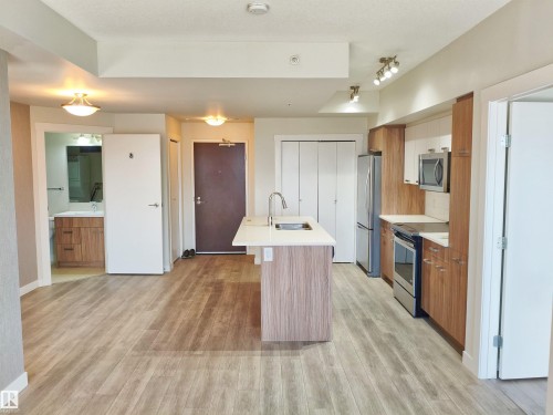 Open-concept living area featuring wood-finish flooring, a kitchen island with integrated sink, stainless steel appliances, modern cabinetry, and a bathroom vanity with under-sink storage - 2505 10410 102 Avenue, Edmonton, AB 