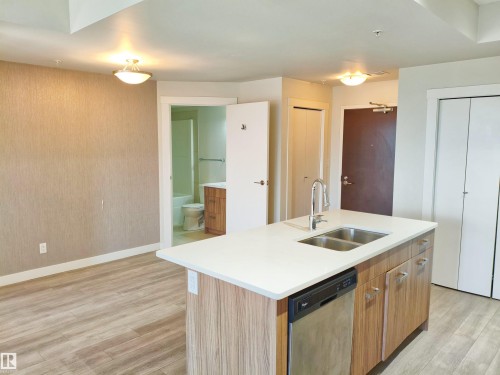 Kitchen island featuring a double-basin stainless steel sink with a high-arc faucet, integrated dishwasher, and wood-finish cabinetry - 2505 10410 102 Avenue, Edmonton, AB 