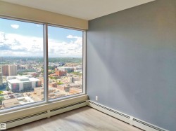 Floor-to-ceiling windows overlooking a cityscape, light wood-finish flooring, and light gray wall paint - 