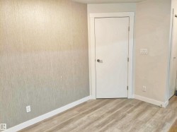 Crisp white door with contrasting hardware, light wood-finish flooring, and textured wall covering - 