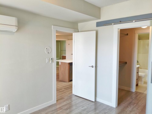 Bright room with light wood-finish flooring, featuring a white barn door on a grey track, and a white interior door - 2505 10410 102 Avenue, Edmonton, AB 
