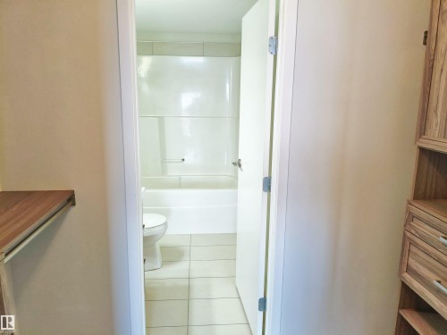 Bathroom featuring a white bathtub and shower surround, white toilet, and light-toned tile flooring - 2505 10410 102 Avenue, Edmonton, AB 