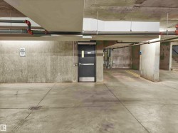 Concrete parking garage with exposed overhead piping, a dark security door, and a visible floor drain - 