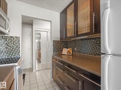 Kitchen featuring dark wood-finish cabinetry with glass-front upper cabinets, a tiled backsplash, and solid surface countertops - 
