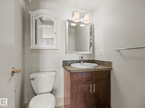 Bathroom featuring a wood-finish vanity with an integrated sink, mosaic tile backsplash, and a contemporary wall-mounted light fixture - 1601 9725 106 Street, Edmonton, AB 