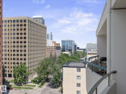 Curved balcony with metal railing featuring city buildings, tree-lined streets, and a clear sky - 