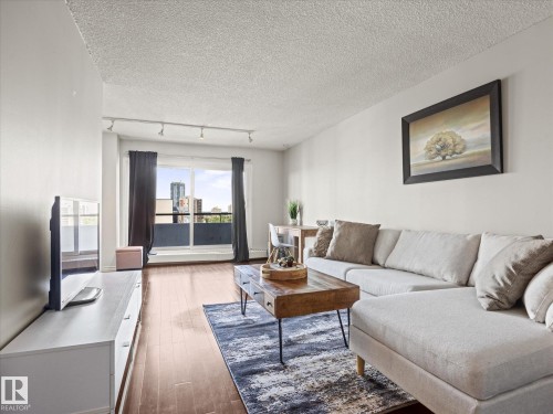 Living space featuring wood-finish flooring, light-colored walls, and a large window with sliding door access to an exterior balcony - 1601 9725 106 Street, Edmonton, AB 