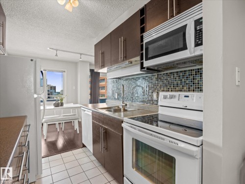 Kitchen featuring white appliances, dark wood-finish cabinetry, mosaic tile backsplash, and a window - 1601 9725 106 Street, Edmonton, AB 