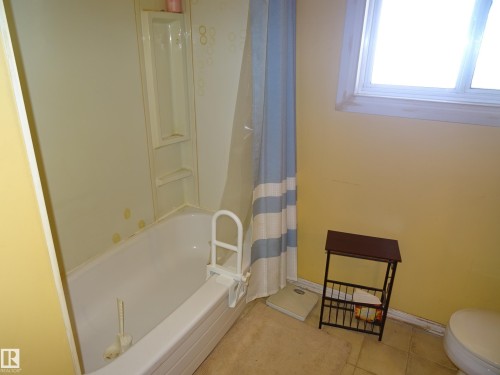 Bathroom featuring a white bathtub with a built-in shower surround and wall-mounted shelving - 5036 52 Street, Andrew, AB 