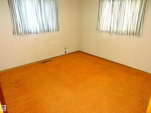 Room with orange carpet flooring, baseboards, and two windows - 5036 52 Street, Andrew, AB 
