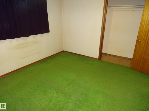Room featuring green carpeting, white wall finishes, and a dark window covering - 5036 52 Street, Andrew, AB 