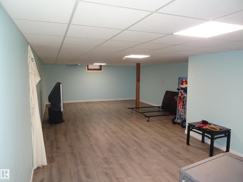 Spacious room featuring wood-finish flooring, light blue walls, and a white grid-patterned ceiling with integrated lighting panels - 5036 52 Street, Andrew, AB 