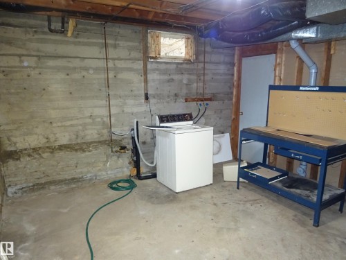 Unfinished basement space featuring exposed concrete walls and ceiling joists, a small window opening, and a concrete floor - 5036 52 Street, Andrew, AB 