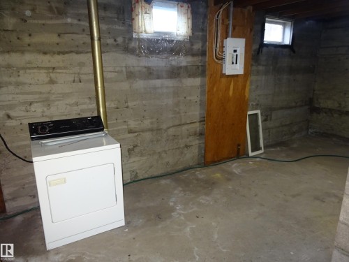 Basement area featuring exposed concrete walls and flooring, a visible electrical panel on a wood panel, and small windows providing natural light - 5036 52 Street, Andrew, AB 