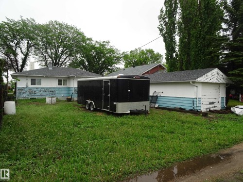 Rear exterior featuring a detached garage and a main structure with a shingled roof - 5036 52 Street, Andrew, AB 