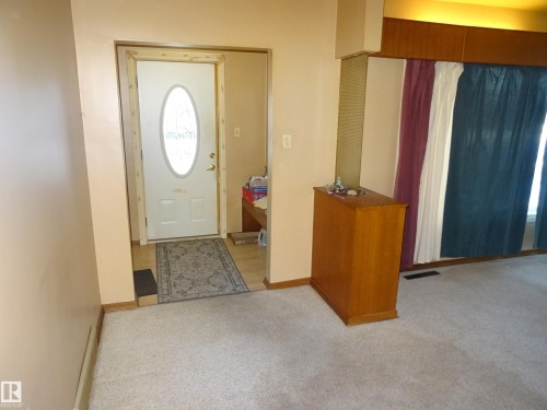 Entryway featuring a white door with an oval glass insert, wood-finish flooring, and light-colored carpeting - 5036 52 Street, Andrew, AB 