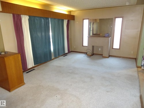 Spacious living area featuring light-colored carpeting and a built-in fireplace structure - 5036 52 Street, Andrew, AB 