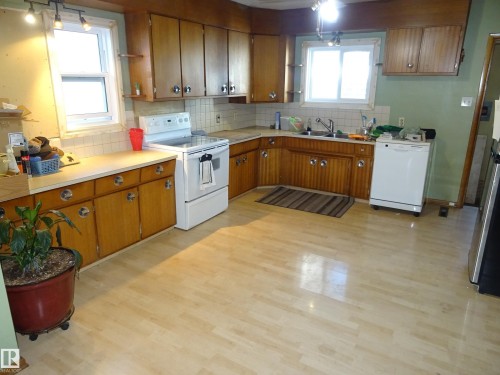 Kitchen featuring wood-finish flooring, two windows, wood cabinetry with circular hardware, white countertops, and a tile backsplash - 5036 52 Street, Andrew, AB 