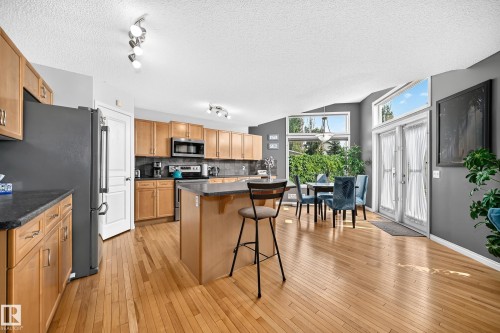 Open-concept kitchen and dining area featuring wood-finish flooring, ample natural wood cabinetry, a central island with a dark countertop, and a stainless steel appliance suite - 8507 179 Avenue, Edmonton, AB 