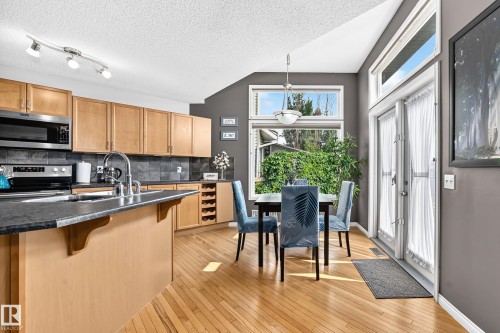 Kitchen and dining area featuring light wood-finish cabinetry, a central island with a dark countertop and integrated sink, stainless steel appliances, and wood-finish flooring - 8507 179 Avenue, Edmonton, AB 
