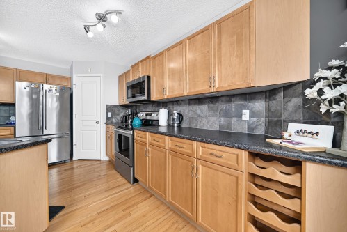 Kitchen featuring wood-finish cabinetry, stainless steel appliances, dark stone-look countertops, and a gray tile backsplash - 8507 179 Avenue, Edmonton, AB 