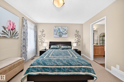 Carpeted bedroom featuring light-toned walls, a decorative ceiling light fixture, and a window with patterned curtains - 8507 179 Avenue, Edmonton, AB 