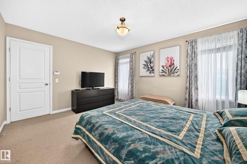 Carpeted bedroom featuring neutral paint, multiple windows with sheers and patterned drapes, a white paneled door, and a flush-mount ceiling light fixture - 8507 179 Avenue, Edmonton, AB 