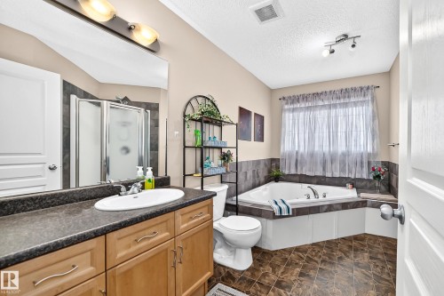 Bathroom featuring a corner soaking tub, a separate glass-enclosed shower, a vanity with a laminate countertop and undermount sink, ceramic tile flooring, and a window with privacy coverings - 8507 179 Avenue, Edmonton, AB 