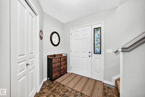 Entryway featuring a paneled door with decorative sidelight, patterned floor tiles, and a built-in closet with bi-fold doors - 8507 179 Avenue, Edmonton, AB 