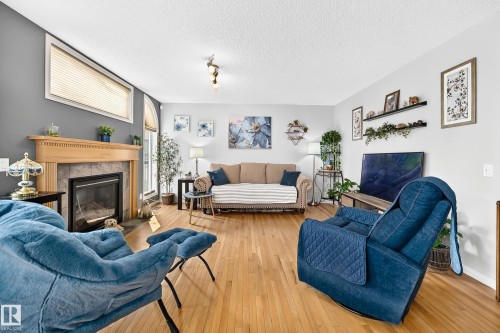 Living area featuring wood-finish flooring and a fireplace with a natural wood mantel and stone surround - 8507 179 Avenue, Edmonton, AB 