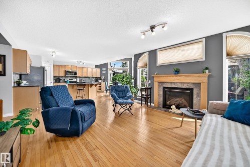 Expansive living area featuring wood-finish flooring, a fireplace with a stone surround and wood mantel, and large windows with arched transoms - 8507 179 Avenue, Edmonton, AB 