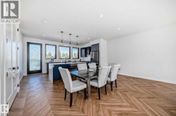 Open-concept living space featuring wood-finish flooring in a herringbone pattern, a kitchen island with seating, pendant lighting, dark cabinetry, and multiple windows - 