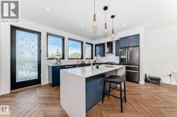 Modern kitchen featuring a large central island with a white countertop, dark blue cabinetry, wood-finish herringbone flooring, stainless steel appliances, and multiple windows - 