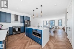 Open-concept kitchen featuring blue cabinetry, white countertops, stainless steel appliances, a white subway tile backsplash, and chevron-patterned wood-finish flooring - 