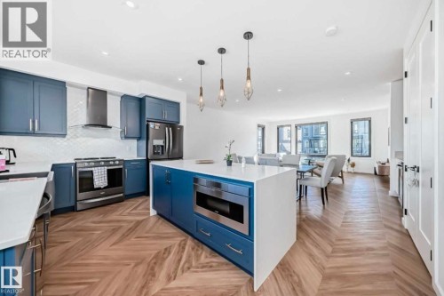 Open-concept kitchen featuring blue cabinetry, white countertops, stainless steel appliances, a white subway tile backsplash, and chevron-patterned wood-finish flooring - 1304 Rutherford Road, Edmonton, AB 