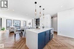 Open-concept living space featuring herringbone wood-finish flooring, a kitchen island with white countertop and blue cabinetry, built-in microwave, and pendant lighting - 