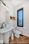 Contemporary bathroom featuring a pedestal sink, white toilet, and wood-finish flooring - 