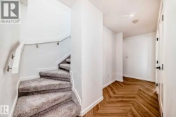Staircase with gray carpeting, white risers, and a white handrail with brushed nickel supports - 