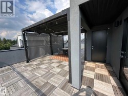 Rooftop terrace featuring wood-finish deck tiles, a black metal pergola with string lighting, and a partially enclosed lounge area with a red-toned tile floor - 
