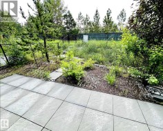 Paved patio area with large format light-toned tiles, featuring a planted garden bed with bark mulch and stepping stones - 