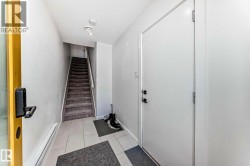 Entryway featuring light-toned tile flooring, a carpeted staircase with white risers and handrail, recessed ceiling lighting, and a white interior door with black hardware - 