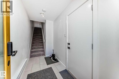 Entryway featuring light-toned tile flooring, a carpeted staircase with white risers and handrail, recessed ceiling lighting, and a white interior door with black hardware - 1304 Rutherford Road, Edmonton, AB 